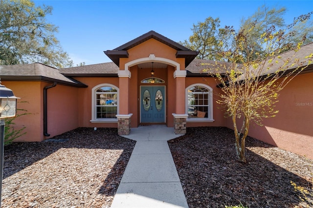 entrance to property featuring a shingled roof and stucco siding