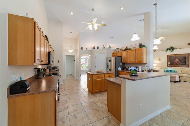 kitchen featuring dark countertops, a center island, light tile patterned floors, stainless steel appliances, and a ceiling fan