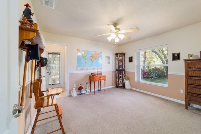 living area with a wealth of natural light, visible vents, carpet floors, and ceiling fan