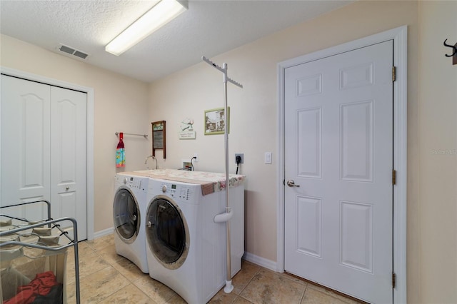 clothes washing area with visible vents, a textured ceiling, separate washer and dryer, light tile patterned floors, and laundry area