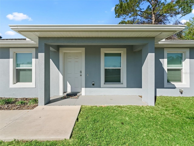 doorway to property with a lawn, a porch, and stucco siding