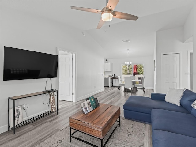 living room with visible vents, ceiling fan with notable chandelier, light wood-style floors, and vaulted ceiling