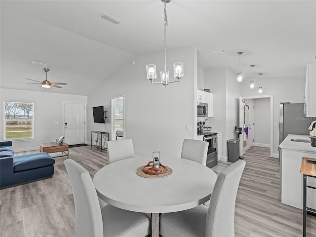 dining area featuring visible vents, light wood-style flooring, ceiling fan with notable chandelier, baseboards, and lofted ceiling