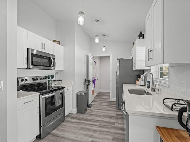 kitchen with lofted ceiling, appliances with stainless steel finishes, light wood-style floors, white cabinets, and a sink