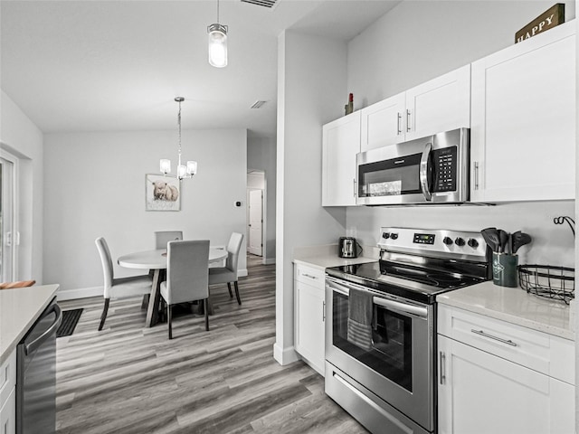 kitchen with decorative light fixtures, light countertops, light wood-style flooring, appliances with stainless steel finishes, and white cabinetry