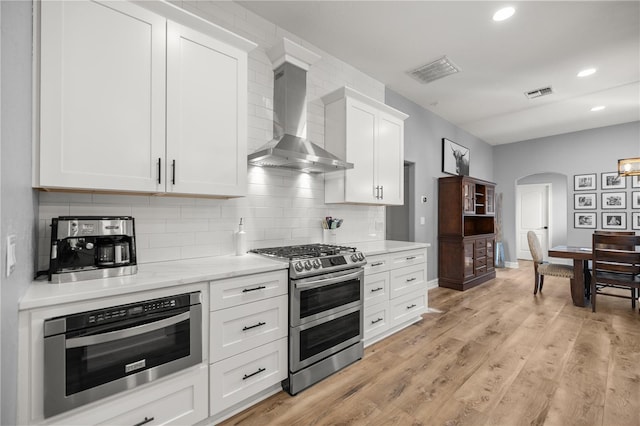 kitchen featuring oven, visible vents, double oven range, arched walkways, and wall chimney exhaust hood