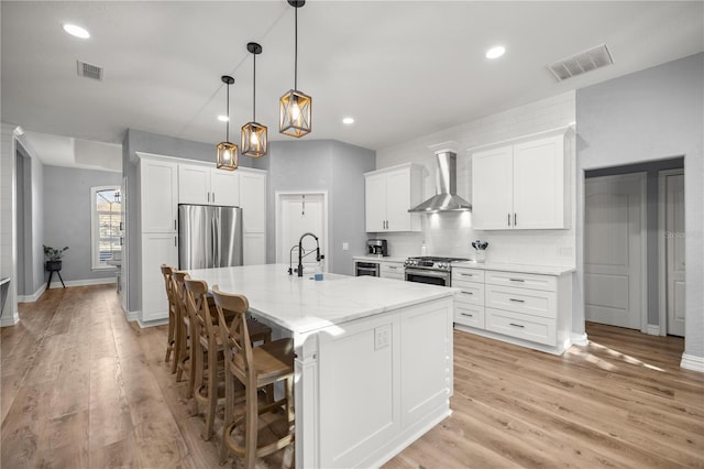 kitchen featuring a sink, stainless steel appliances, visible vents, and wall chimney exhaust hood