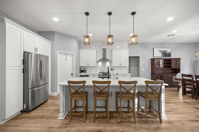 kitchen with light countertops, wall chimney range hood, light wood-style floors, and freestanding refrigerator