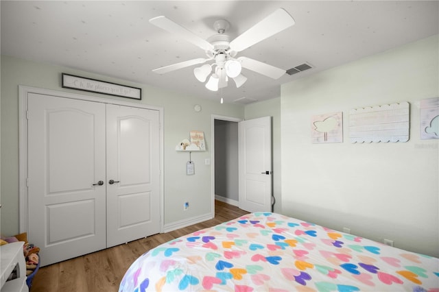 bedroom featuring a ceiling fan, wood finished floors, visible vents, baseboards, and a closet