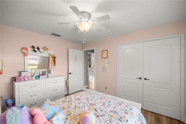 bedroom with a ceiling fan, wood finished floors, visible vents, baseboards, and a closet