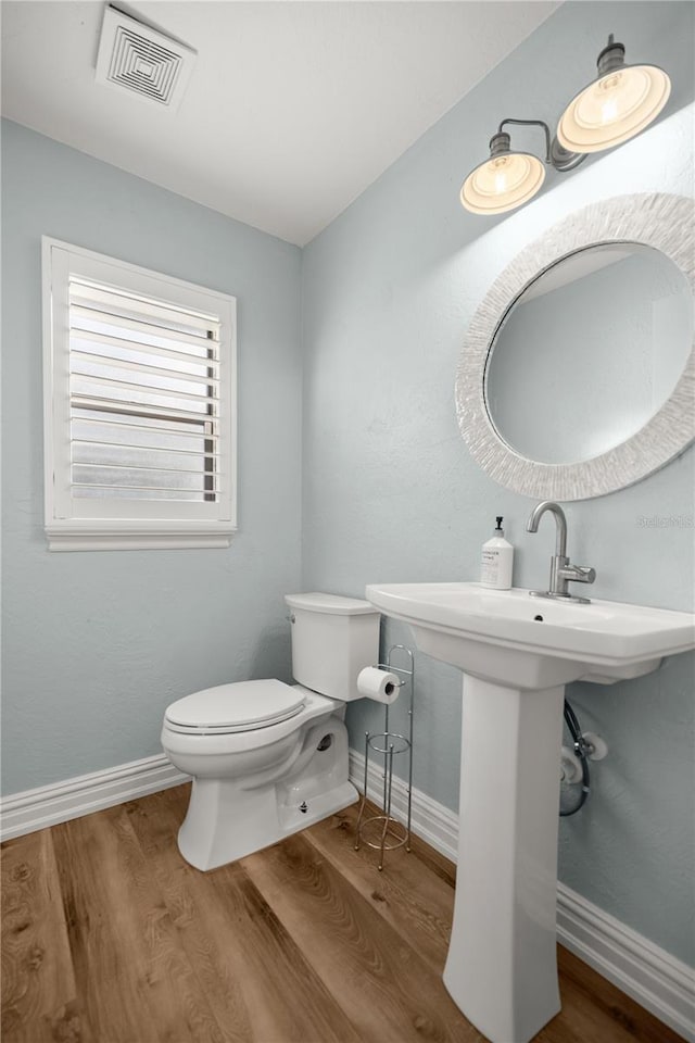 half bath with toilet, wood finished floors, visible vents, and baseboards