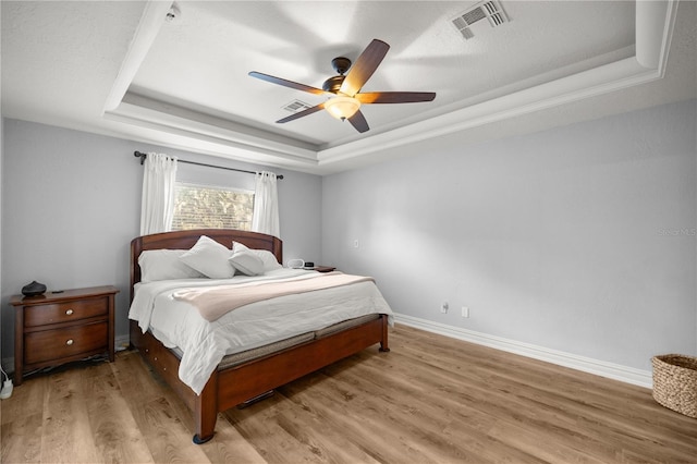 bedroom with baseboards, a raised ceiling, visible vents, and light wood-style flooring