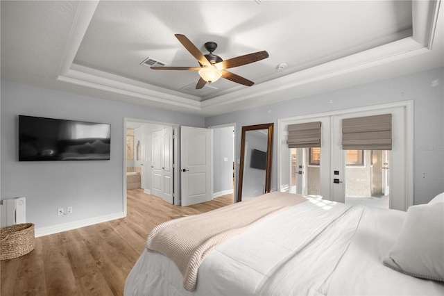 bedroom featuring baseboards, french doors, light wood-style floors, ensuite bathroom, and a raised ceiling