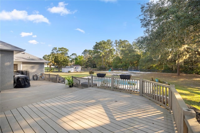 deck with an outbuilding, a pool, fence, a shed, and a lawn