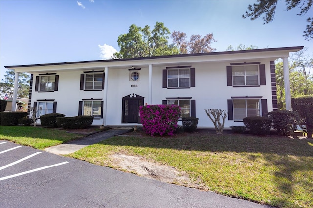 view of front of house featuring stucco siding, uncovered parking, and a front yard