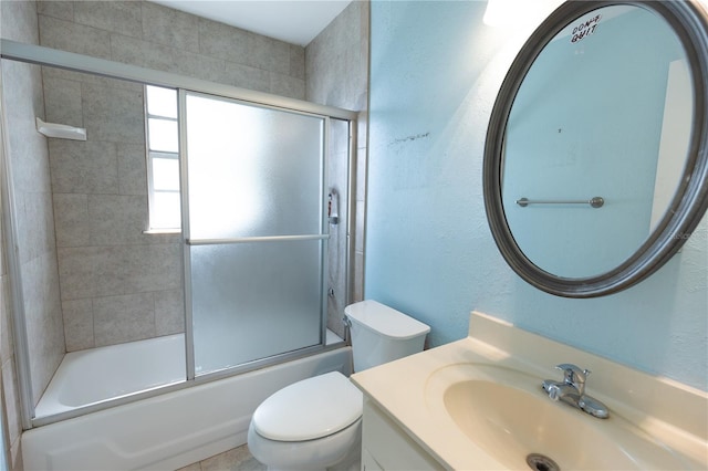 full bathroom featuring vanity, toilet, a textured wall, and combined bath / shower with glass door