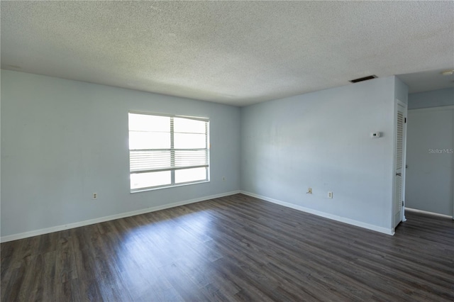 unfurnished room with a textured ceiling, dark wood-style floors, visible vents, and baseboards