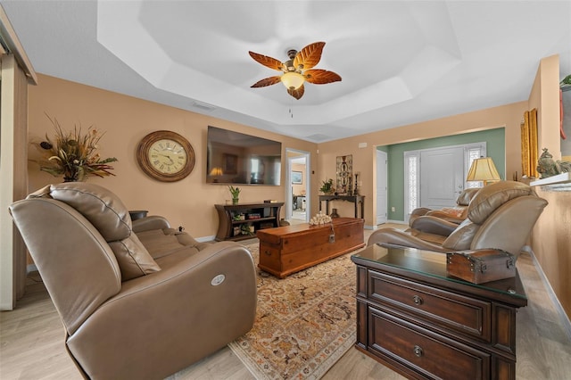 living room featuring a tray ceiling, baseboards, visible vents, and ceiling fan