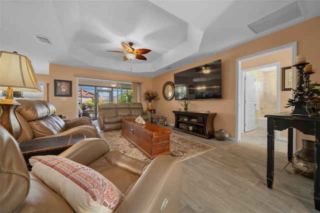 living room featuring visible vents, a raised ceiling, ceiling fan, and light wood finished floors