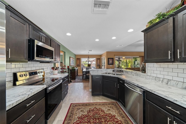 kitchen featuring visible vents, light wood finished floors, a peninsula, a sink, and appliances with stainless steel finishes