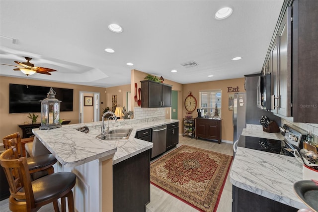 kitchen with visible vents, a breakfast bar, a sink, appliances with stainless steel finishes, and a peninsula