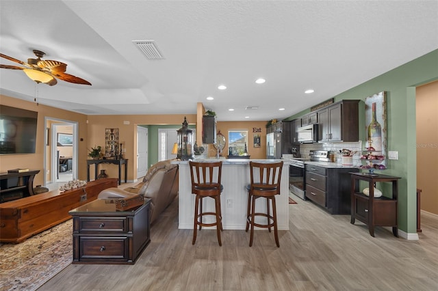 kitchen with visible vents, a ceiling fan, a kitchen breakfast bar, appliances with stainless steel finishes, and light wood finished floors