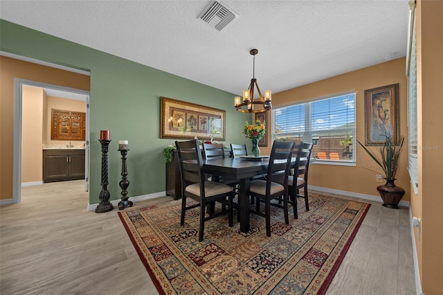 dining room featuring an inviting chandelier, baseboards, visible vents, and light wood-type flooring