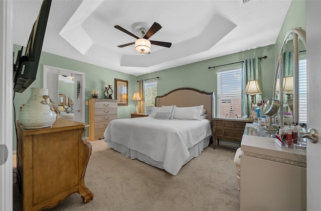 bedroom with light colored carpet, a tray ceiling, and multiple windows