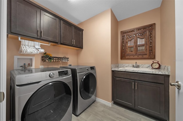 clothes washing area with washer and clothes dryer, cabinet space, baseboards, and a sink