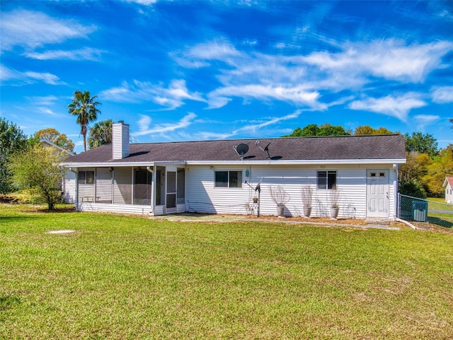 rear view of property featuring fence, a lawn, a chimney, and a sunroom