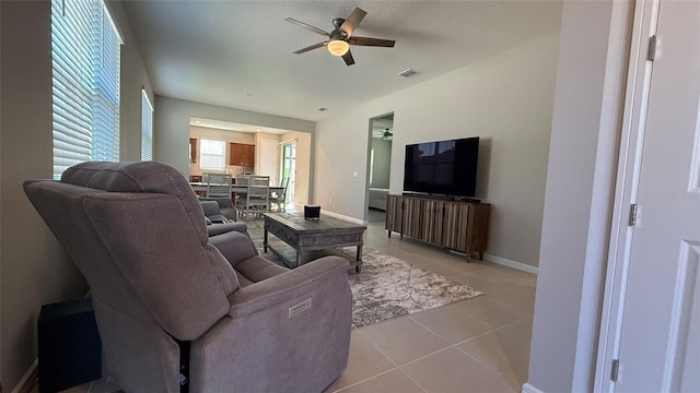 living area featuring light tile patterned floors, visible vents, baseboards, and a ceiling fan