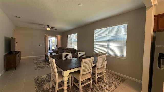 dining area with light tile patterned floors, baseboards, a textured ceiling, and ceiling fan