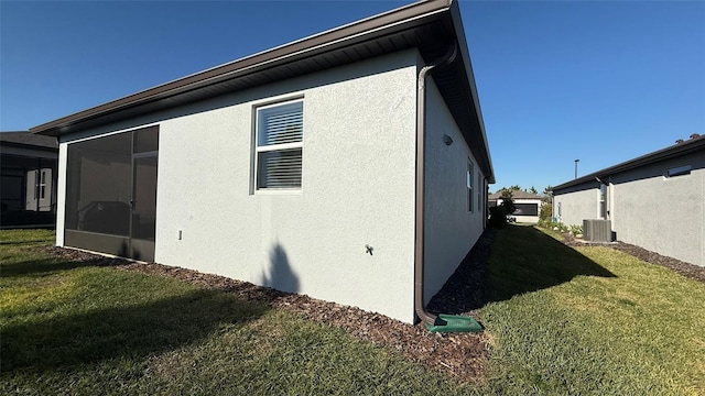 view of side of property featuring a yard, central air condition unit, stucco siding, and a sunroom