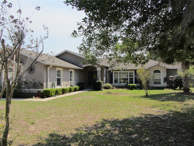 ranch-style home with a shingled roof, a front lawn, and stucco siding