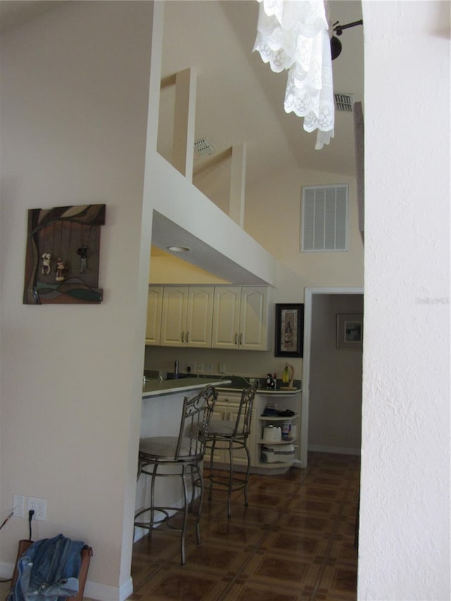 kitchen featuring visible vents, high vaulted ceiling, baseboards, and dark floors