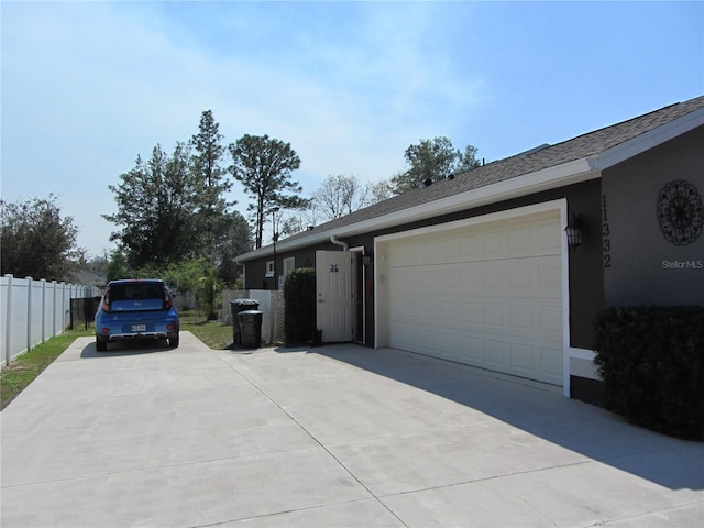 view of side of property featuring stucco siding, concrete driveway, a garage, and fence