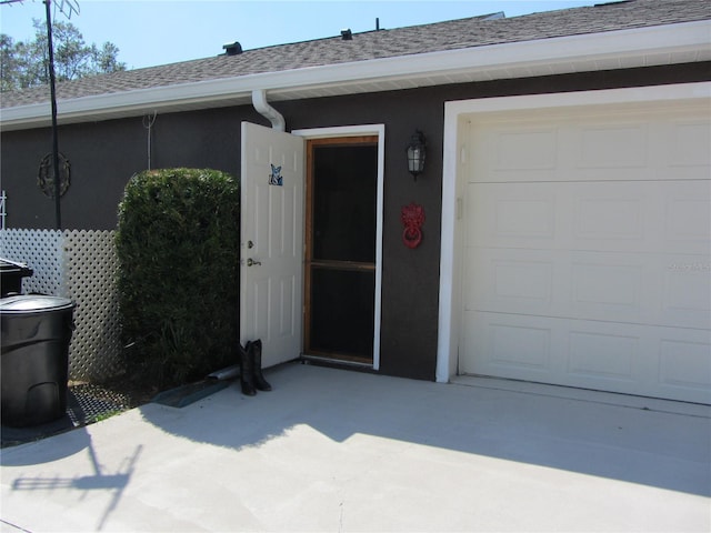 entrance to property with stucco siding, a shingled roof, and a garage