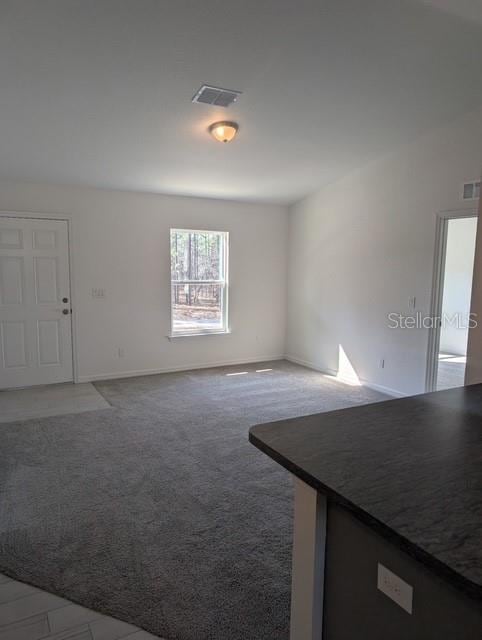 unfurnished living room featuring visible vents, carpet floors, and baseboards