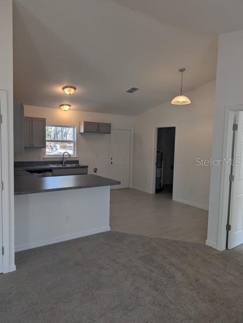 kitchen featuring visible vents, a peninsula, a sink, vaulted ceiling, and light carpet