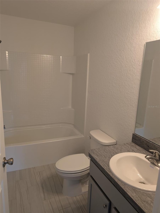 bathroom featuring toilet, vanity, bathtub / shower combination, and a textured wall