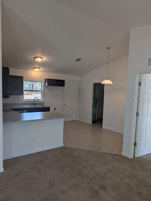 kitchen featuring visible vents, decorative light fixtures, a peninsula, light colored carpet, and vaulted ceiling