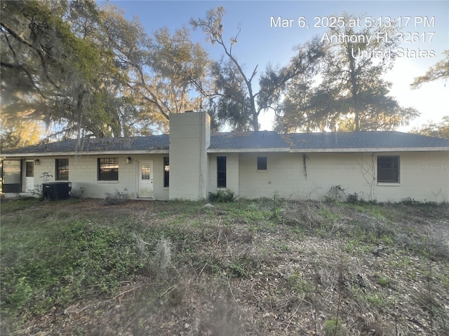 back of house with a chimney, central air condition unit, and concrete block siding