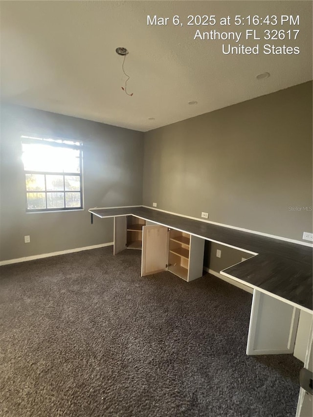 unfurnished office featuring dark carpet and baseboards