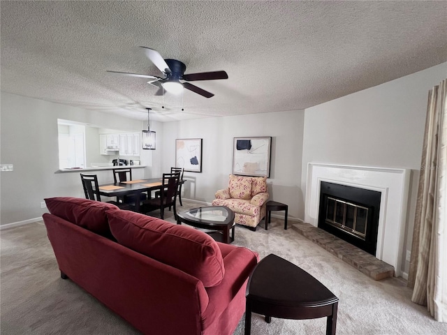 living area with a ceiling fan, baseboards, a fireplace, a textured ceiling, and light carpet