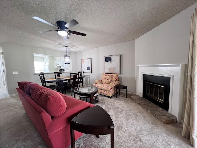 living room featuring a glass covered fireplace, a textured ceiling, carpet floors, and ceiling fan