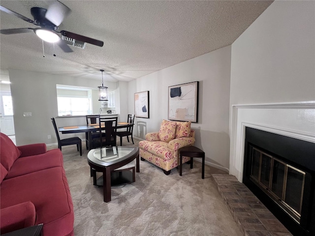 carpeted living area with baseboards, a textured ceiling, a brick fireplace, and a ceiling fan