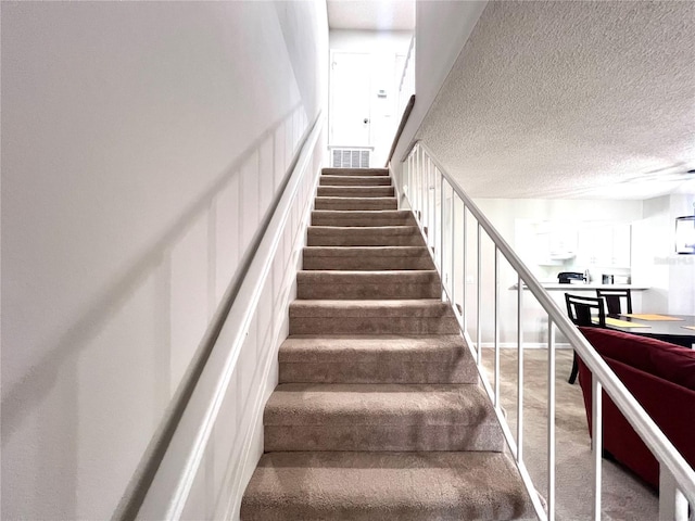 stairway featuring visible vents, a textured ceiling, and carpet