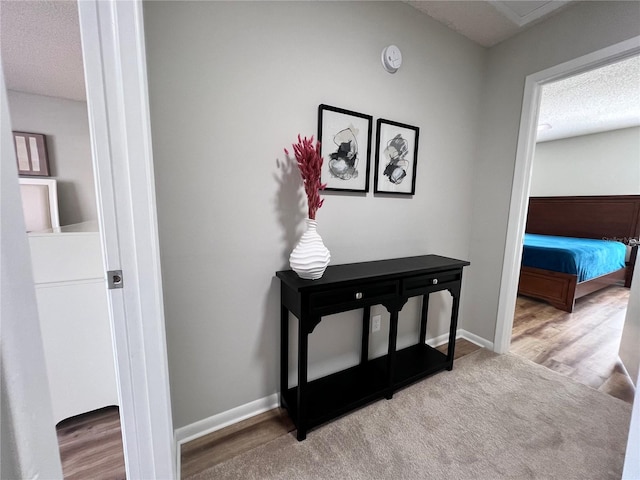 corridor featuring wood finished floors, baseboards, and a textured ceiling