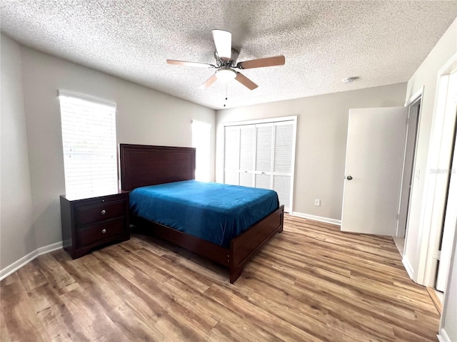 bedroom with a textured ceiling, wood finished floors, a closet, and baseboards