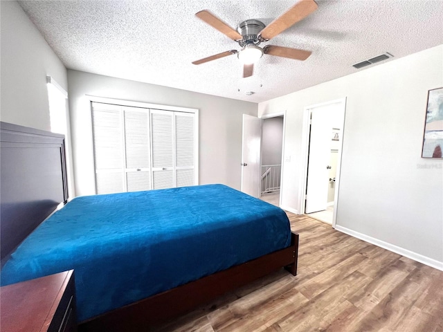 bedroom with wood finished floors, visible vents, baseboards, ceiling fan, and a textured ceiling